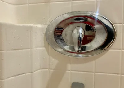 Close-up of a shiny chrome shower control against a tiled wall, with water droplets hinting at recent use.