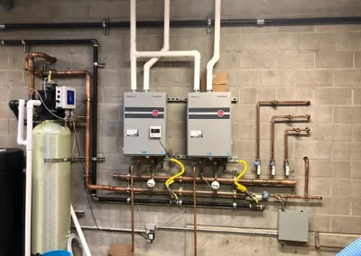 A wall-mounted plumbing setup featuring two tankless water heaters, copper pipes, and a water filtration system.