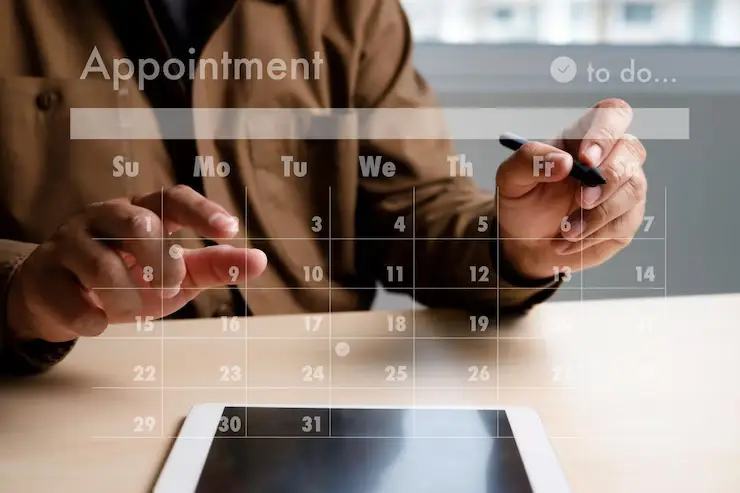 A person is using a stylus on a tablet with a digital calendar overlay, planning appointments for the week ahead.